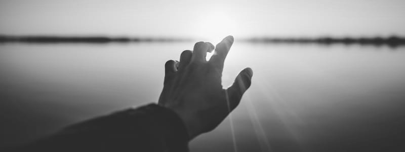 A hand reaching towards the sun over the horizon.